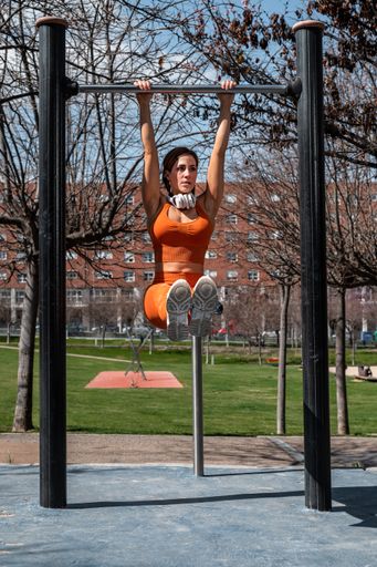 A Attractive sporty woman with headphones around her neck doing stretching and balance exercises while hanging on a bar in an urban setting