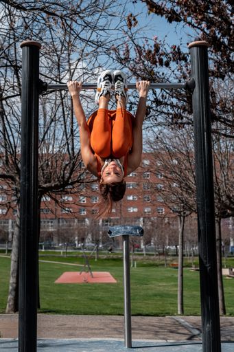A Attractive sporty woman with headphones around her neck doing stretching and balance exercises while hanging on a bar in an urban setting