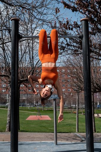 A Attractive sporty woman with headphones around her neck doing stretching and balance exercises while hanging on a bar in an urban setting