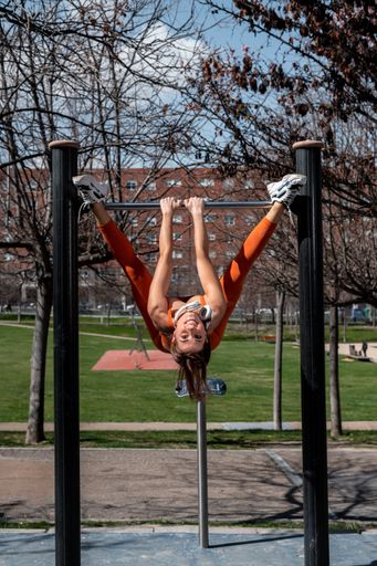 A Attractive sporty woman with headphones around her neck doing stretching and balance exercises while hanging on a bar in an urban setting