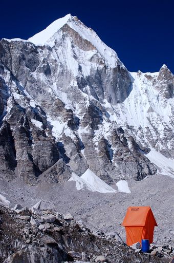 A vertical shot of a mountain covered in snow with an orange tent in front of it