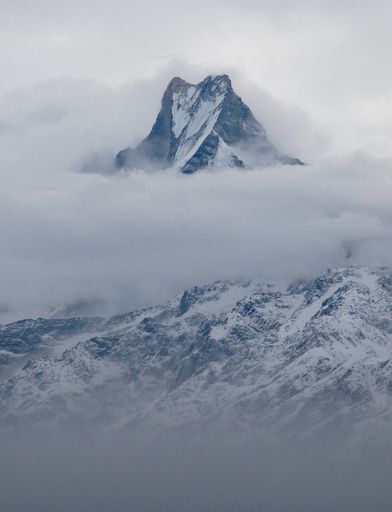 A vertical shot of a beautiful mountain covered with snow on a foggy day