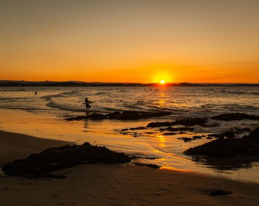 A wide shot of the beautiful sea waves and a female holding a surfboard during sunset