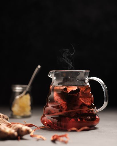 A vertical closeup shot of a glass of tea with leaves on the side on a black background