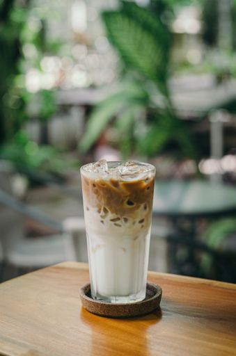 A vertical shot of a latte with ice on a wooden surface and a blurred background