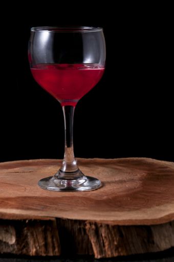 A vertical shot of a glass of a red drink on a wooden surface