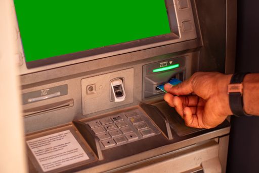 A close-up shot of a hand putting his card in the atm with a green screen display