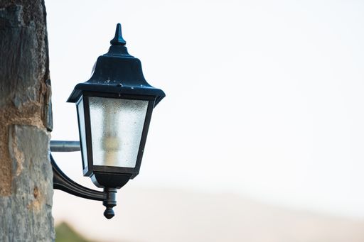 A vertical shot of a black street lantern hanging on a wooden pole against bright sky during daytime