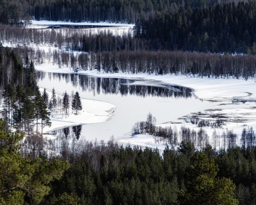 An aerial view of a peaceful snowy landscape with frozen lake and forests during winter