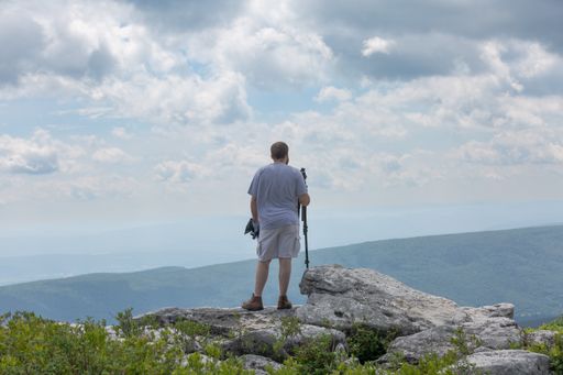 A rear view of a man carrying a photography tripod at the Bear Rocks in Dolly Sods, WV