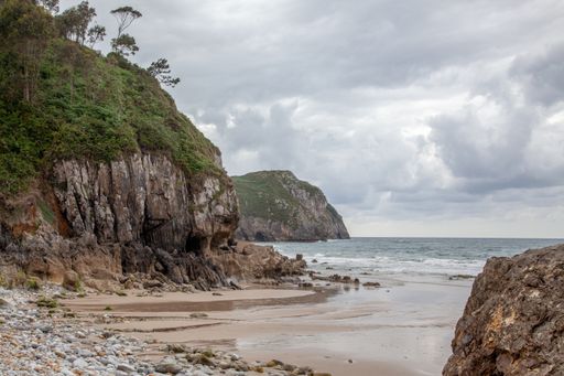 A beautiful view of a sandy beach with many rocks and splashing sea waves under a cloudy sky