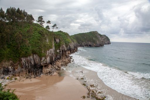 A beautiful view of a sandy beach with many rocks and splashing sea waves under a cloudy sky