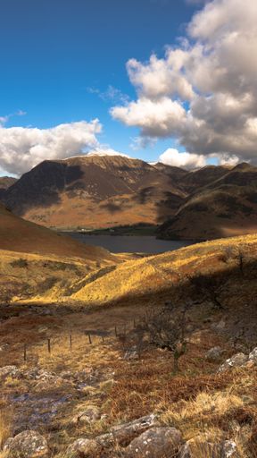 A vertical shot of a dry valley with the small lake and hills on a cloudy day