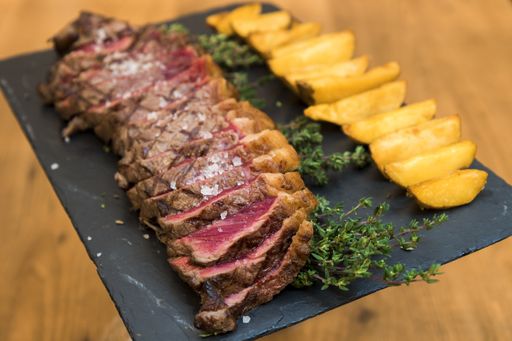 A shallow focus closeup shot of cut up steak and potatoes with herbs and rock salt on a black cutting board