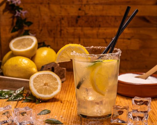 A shallow focus shot of a glass of lemonade with ice cubes, plastic straws, lemon slices, and sugar