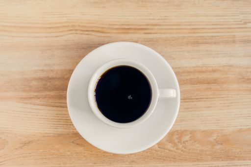 A white cup of dark coffee put on the wooden surface