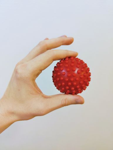 A vertical shot of a hand holding a massage ball on white wall background.