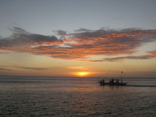 A wide shot of a boat on the body of the sea under a cloudy sky during sunset