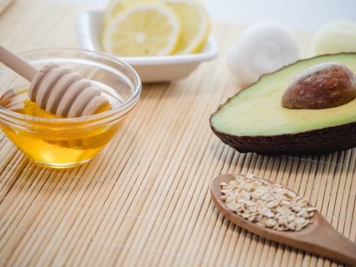 A closeup shot of natural skincare product ingredients: avocado, honey, oat flakes, and lemon