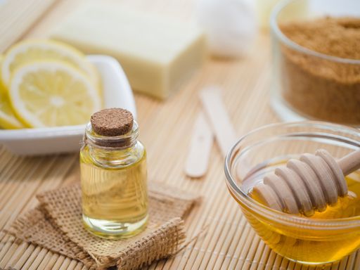 A closeup shot of natural skincare product ingredients: lemon, honey, and brown sugar and essential oil