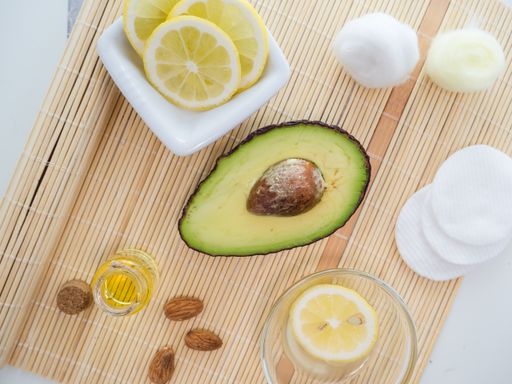 An overhead shot of natural skincare product ingredients: lemon, essential oil, almonds, and avocado