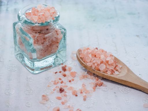 A closeup shot of a jar and a wooden spoon with pink sea salt