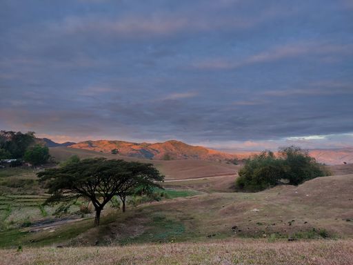 A beautiful view of hills with trees under the cloudy sky at sunset