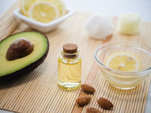 A closeup shot of natural skincare product ingredients: avocado, almonds, lemon, and essential oil