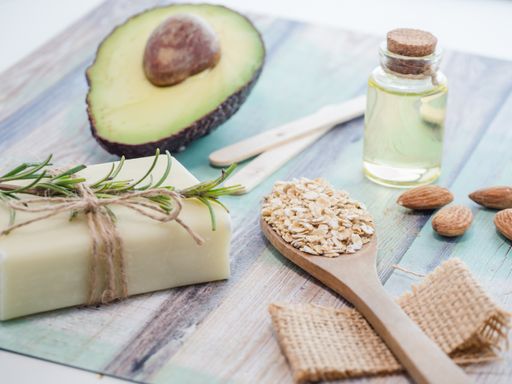 A closeup shot of natural skincare product ingredients: avocado, almonds, natural soap, essential oil, and oat flakes