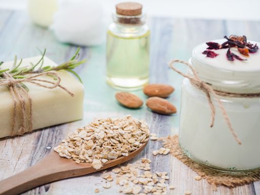 A closeup shot of natural skincare product ingredients: natural soap, oat flakes, yogurt, almonds, and essential oil