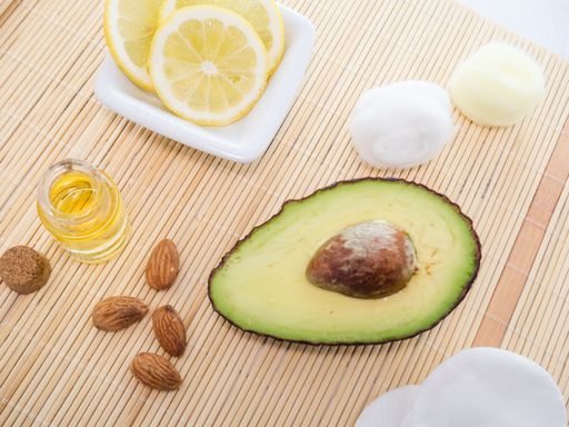 An overhead shot of natural skincare product ingredients: lemon, essential oil, almonds, and avocado