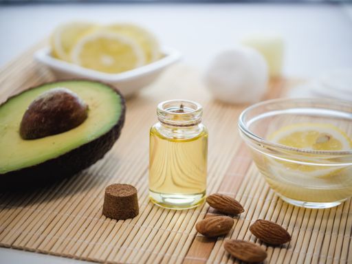 A closeup shot of natural skincare product ingredients: lemon, avocado, almonds, and essential oil