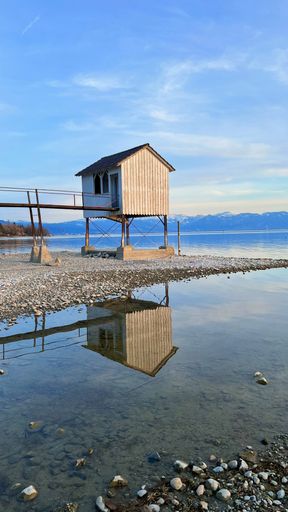 A vertical shot of a wooden cabin by the lake with the beautiful blue sky in the background