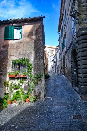A vertical shot of a narrow cobblestone street with old buildings. Anguillara Sabazia, Lazio, Italy.