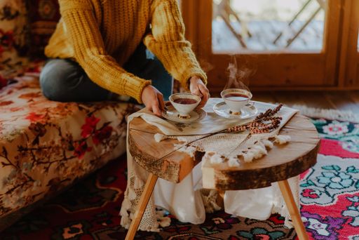 Two cups of tea on a wooden small table with a Caucasian woman, sitting on a couch, taking one to drink