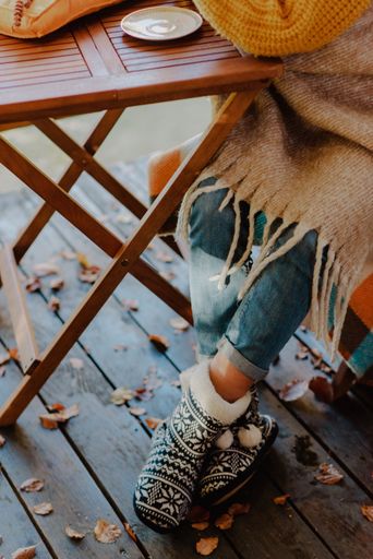 A vertical shot of a girl wearing stylish clothes and soft Christmas boots, sitting next to a wooden table