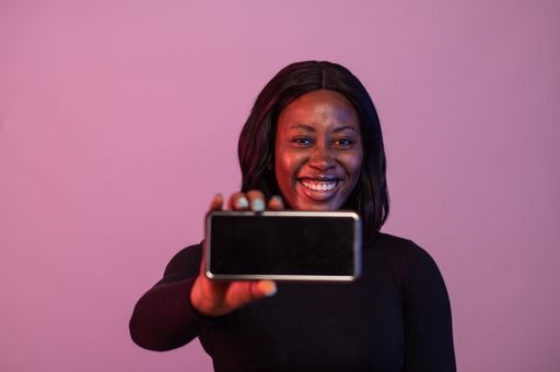 A cheerful Nigerian woman showing her phone screen isolated on pink background