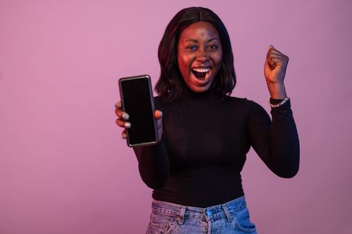An excited Nigerian woman showing phone screen isolated on pink background
