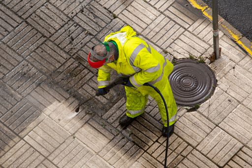 Worker cleaning a street sidewalk with high pressure water jet machine. Cleaning public spaces