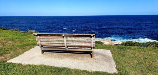 A panoramic shot of a bench near the sea under a blue clear sky