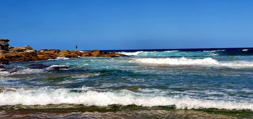 A panoramic shot of cliffs near the sea under a blue cloudy sky