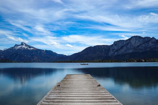 A beautiful landscape view of a wooden pier on the lake against mountains and blue cloudy sky