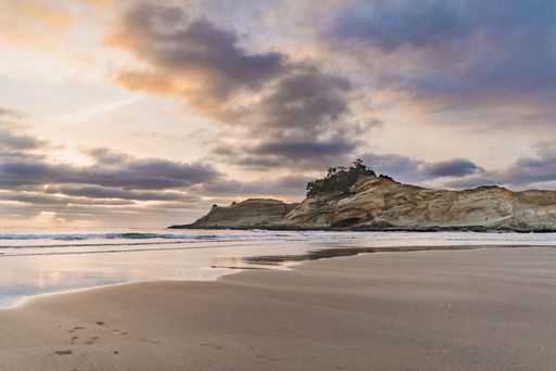 A beautiful wide shot of a cliff by the sea with a sandy shore under a sky with clouds