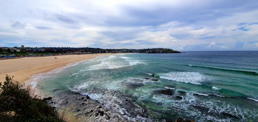 A panoramic shot of a seashore near the sea under a blue cloudy sky