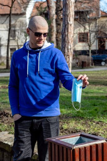 A young man in the park throwing away a protective face mask into the trash bin. Covid-19 pandemic crisis end.