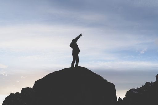 A wide silhouette shot of a person standing on a cliff under a clear blue sky