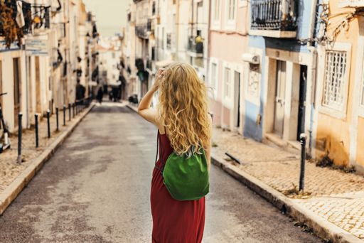 A young female tourist in a red dress walking through a road surrounded by buildings under the sunlight