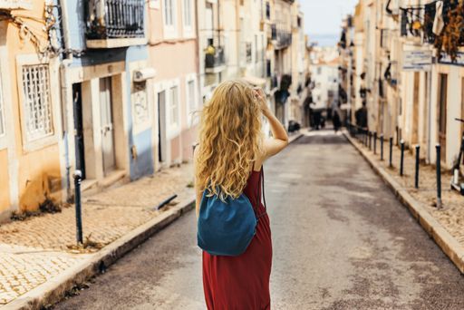 A young female tourist in a red dress walking through a road surrounded by buildings under the sunlight