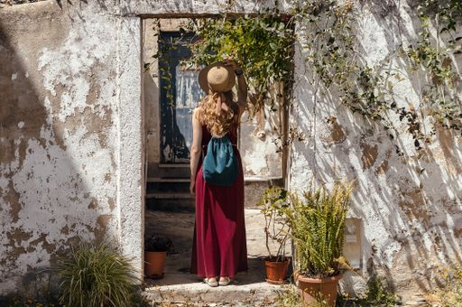 A young female with a hat on in a red dress standing on the doorway of an old building