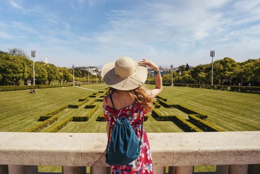 A young female tourist in a red floral dress in The Eduardo VII Park under the sunlight in Portugal